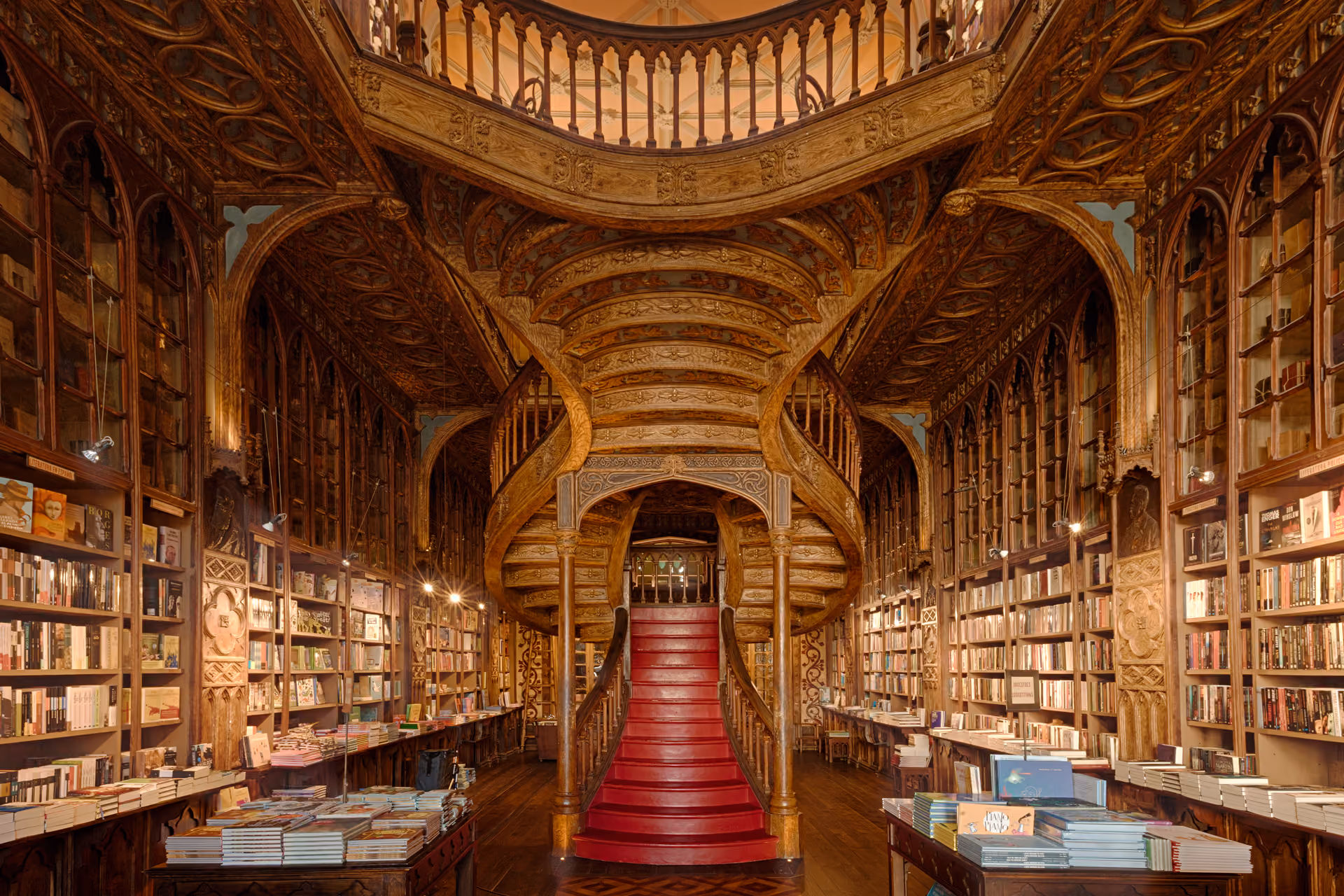 Interior da Livraria Lello, com estantes de madeira repletas de livros e a icónica escadaria central ornamentada.