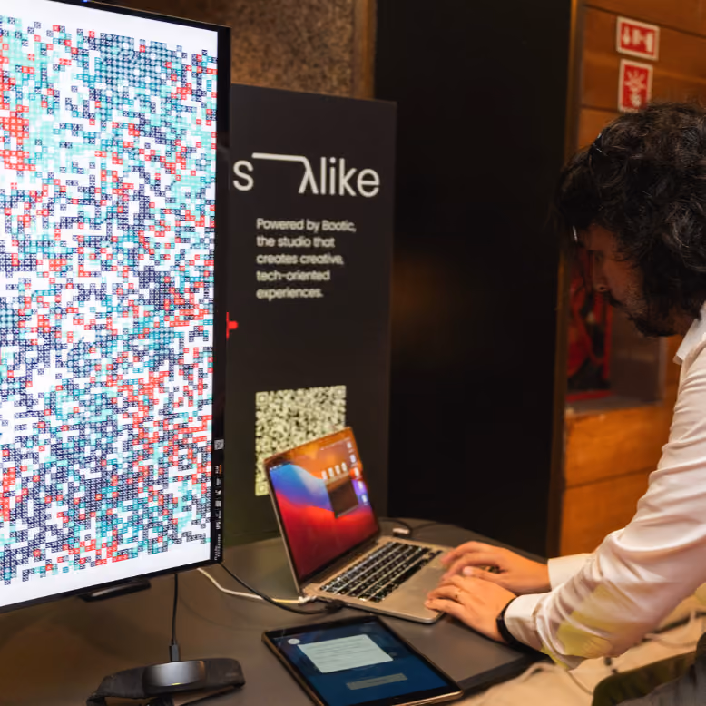 Fernando Lopes utiliza um computador portátil e um tablet junto a um monitor que apresenta o poster colorido gerado pelo FRQNCY, uma experiência desenvolvida pela Bootic.