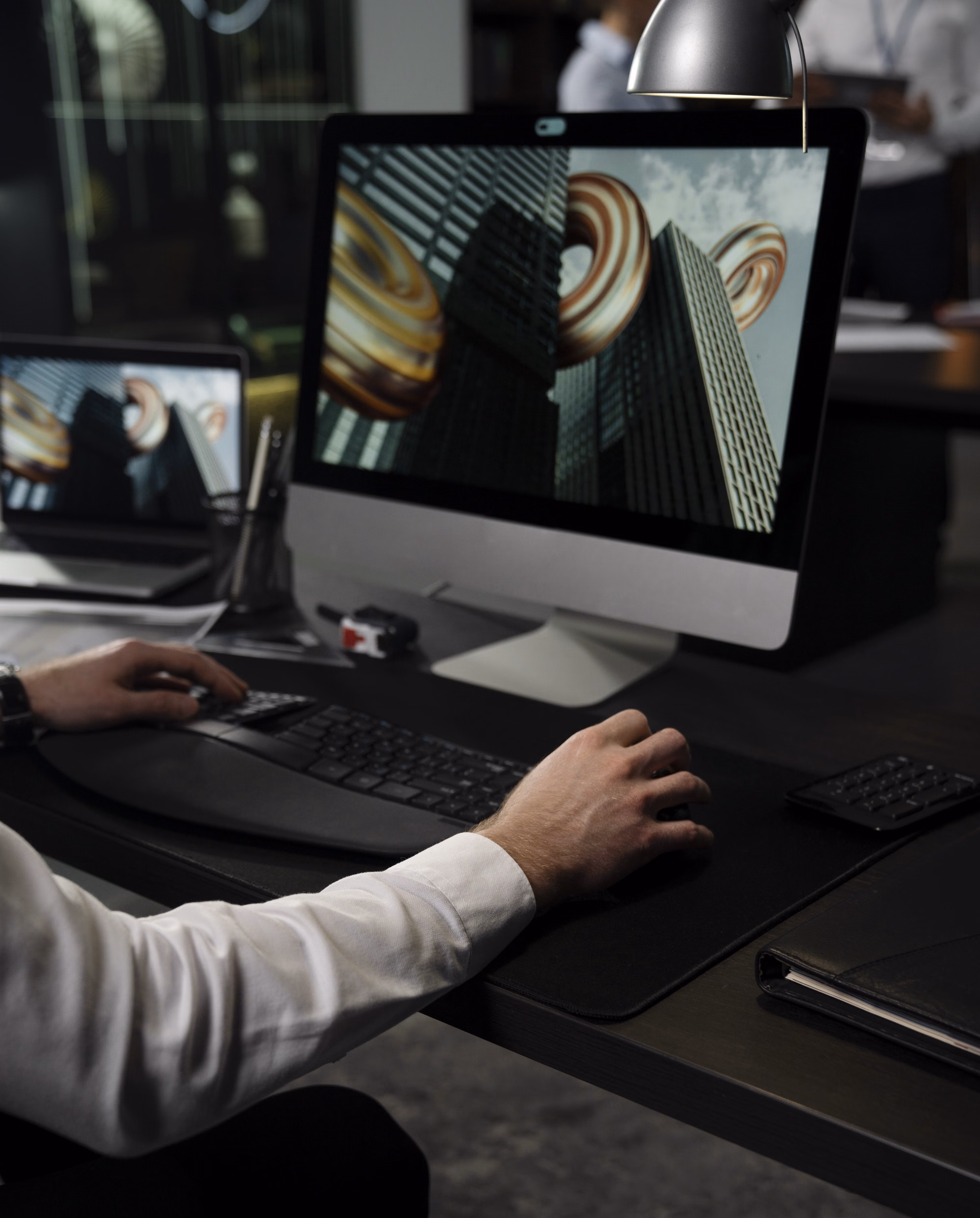 Pessoa trabalha num computador com um modelo 3D de edifícios e formas esféricas às riscas apresentado no ecrã.